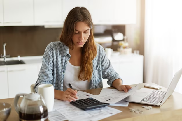 Woman working on finances at table with computer and calculator.